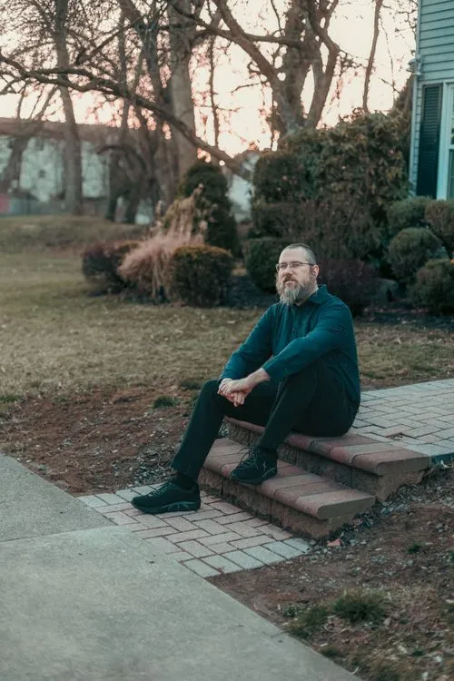Aaron Silverman sitting on brick steps in a front yard, looking toward the camera.